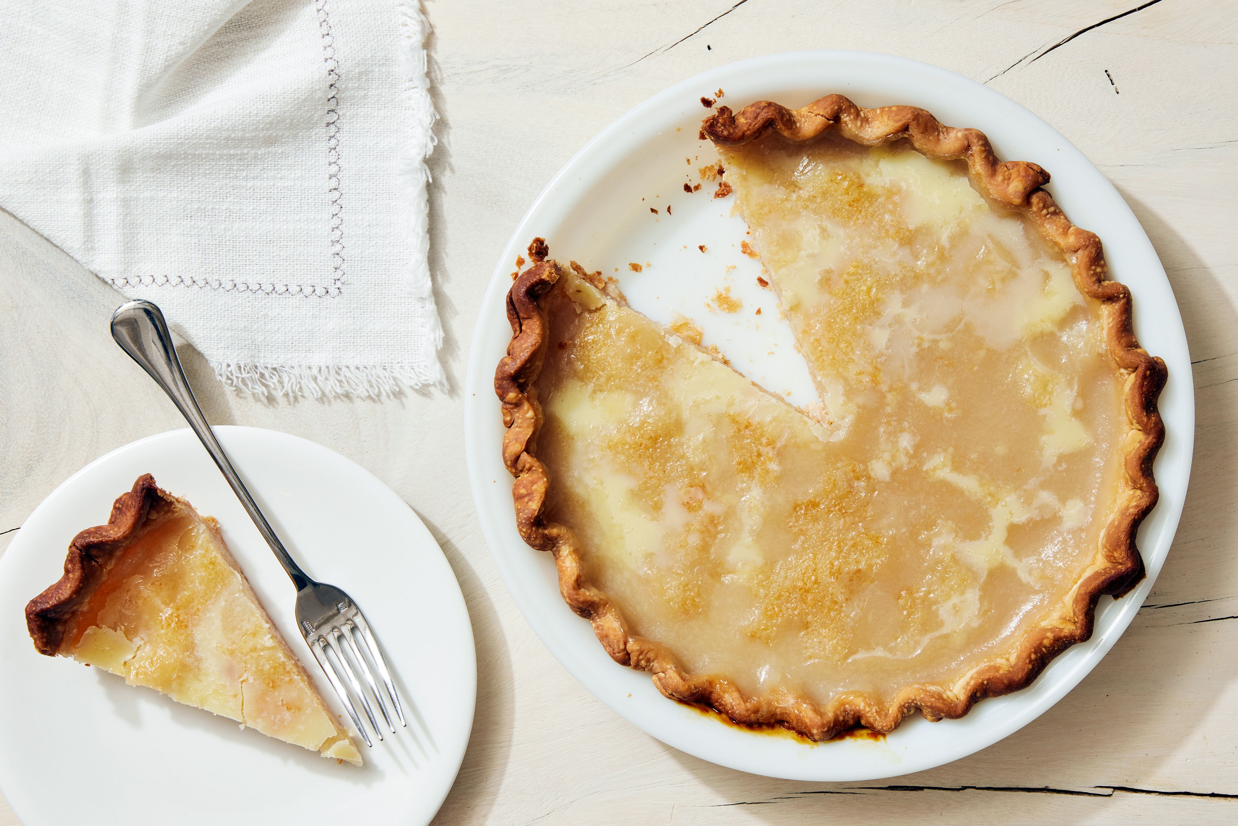 A single slice of water pie on a small dessert plate, showing a glossy, custard-like filling and flaky golden crust on a wooden table in warm kitchen light