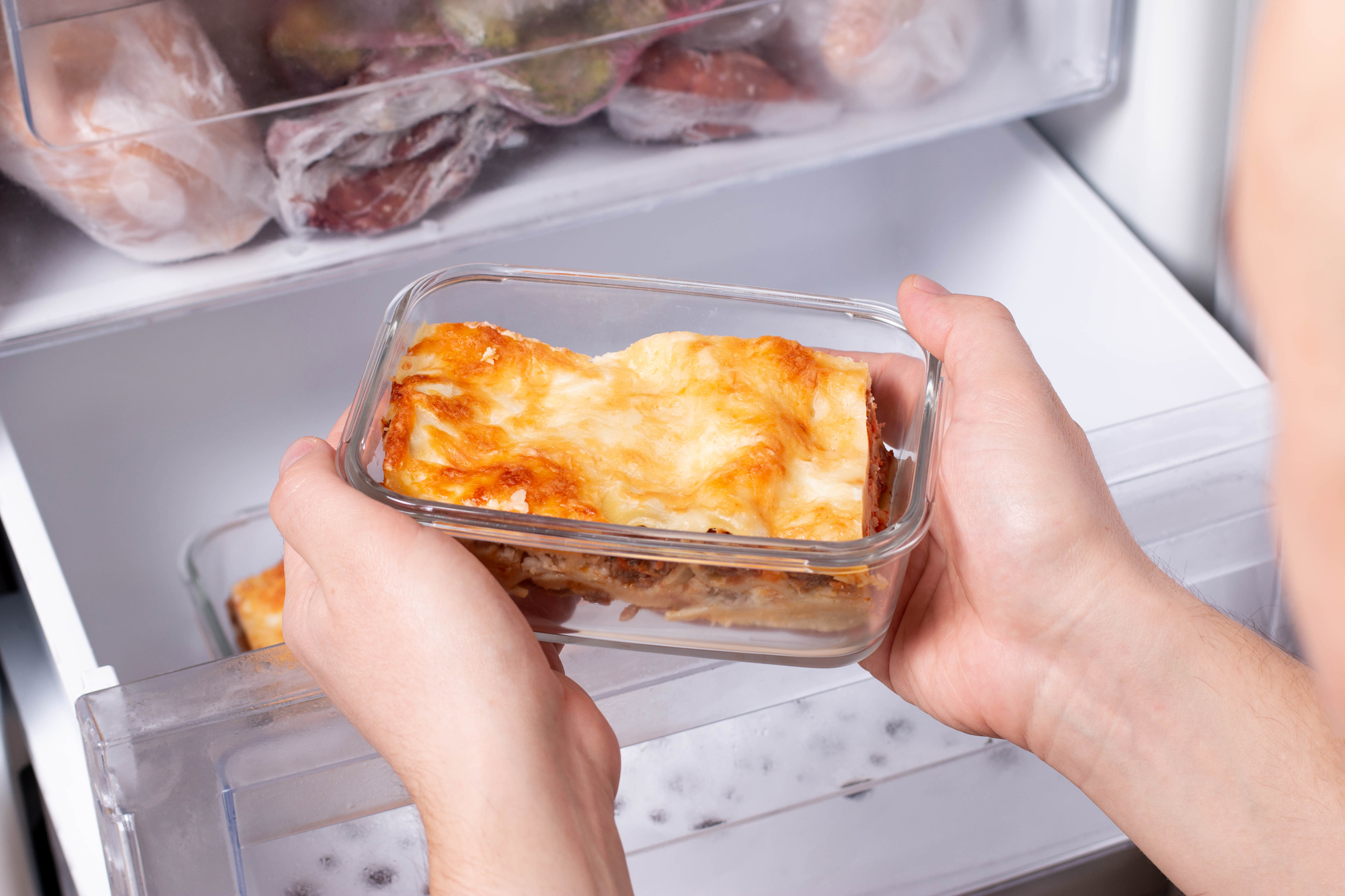 A single square of leftover ravioli lasagna in a glass meal prep container with a fork beside it on a kitchen counter