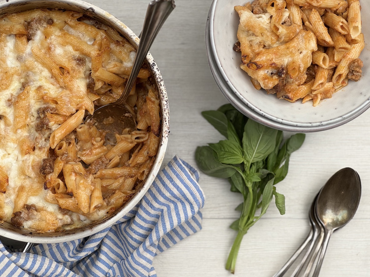 A skillet filled with cheesy beefaroni, topped with melted cheddar and a sprinkle of parsley, sitting on a warm-toned kitchen counter with soft natural light