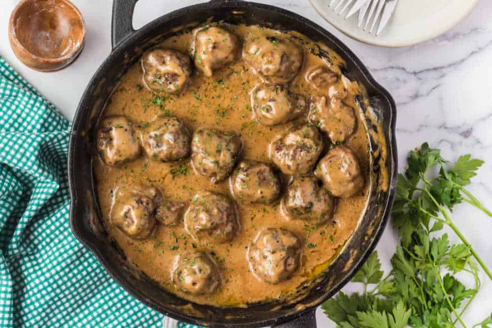 A skillet filled with creamy Swedish meatball sauce spooned over browned meatballs, steam rising in a warm home kitchen