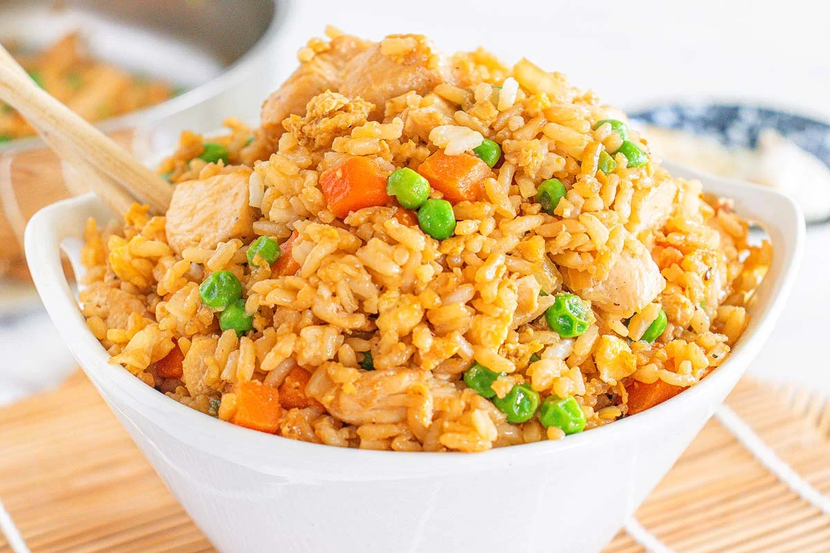 A skillet of chicken fried rice with peas, scrambled egg, and scallions, with crisp browned rice grains visible, on a warm kitchen counter