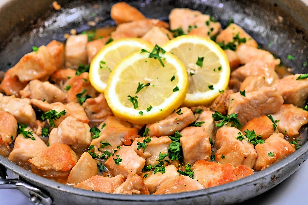 A skillet of chicken scampi with golden seared chicken pieces in a glossy lemon garlic butter sauce, sprinkled with parsley, on a stovetop under warm kitchen lighting
