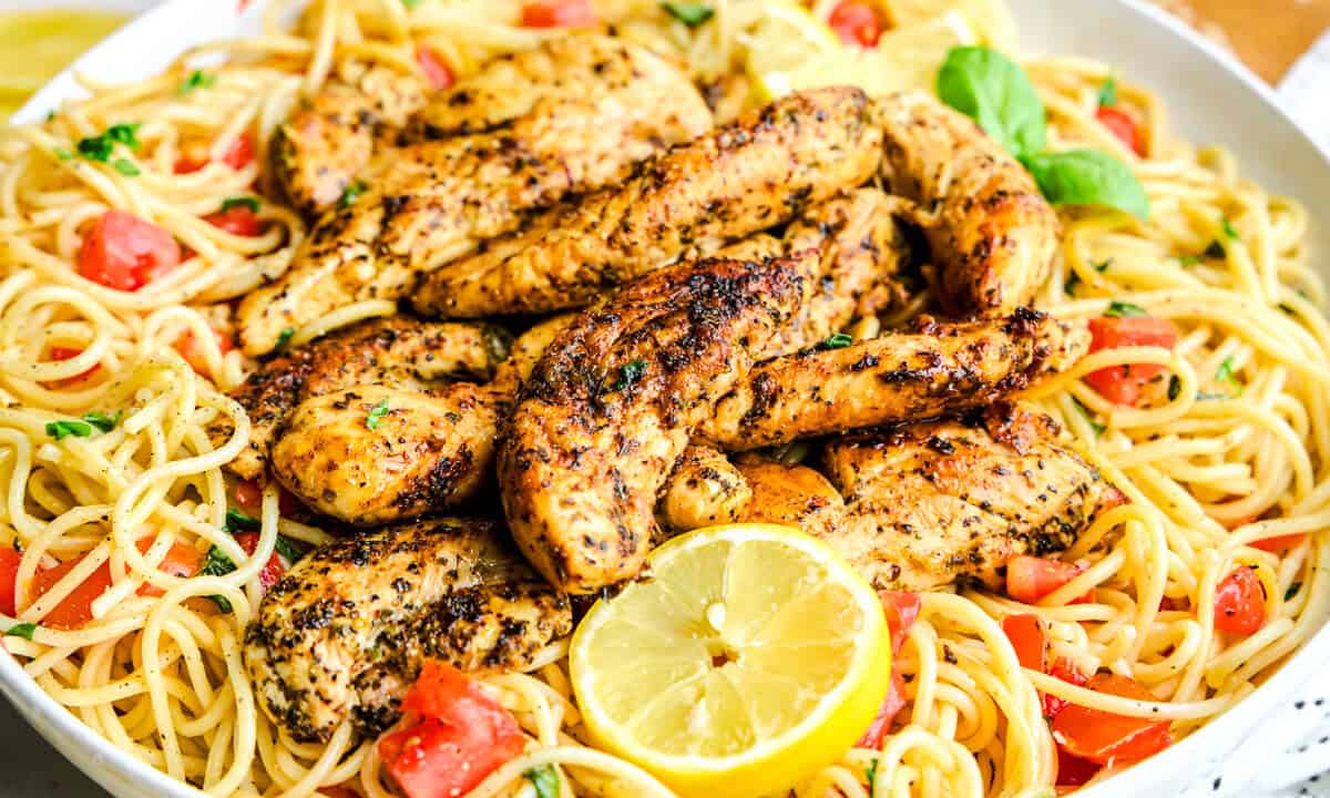 A skillet of creamy lemon herb chicken pasta with golden seared chicken pieces, parsley, and lemon slices on top, on a warm kitchen counter with soft natural light