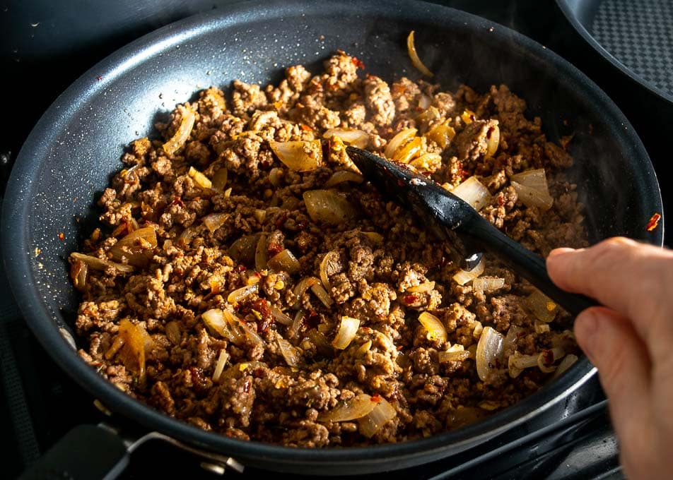 A skillet of seasoned ground beef with onions and spices simmering with a little sauce