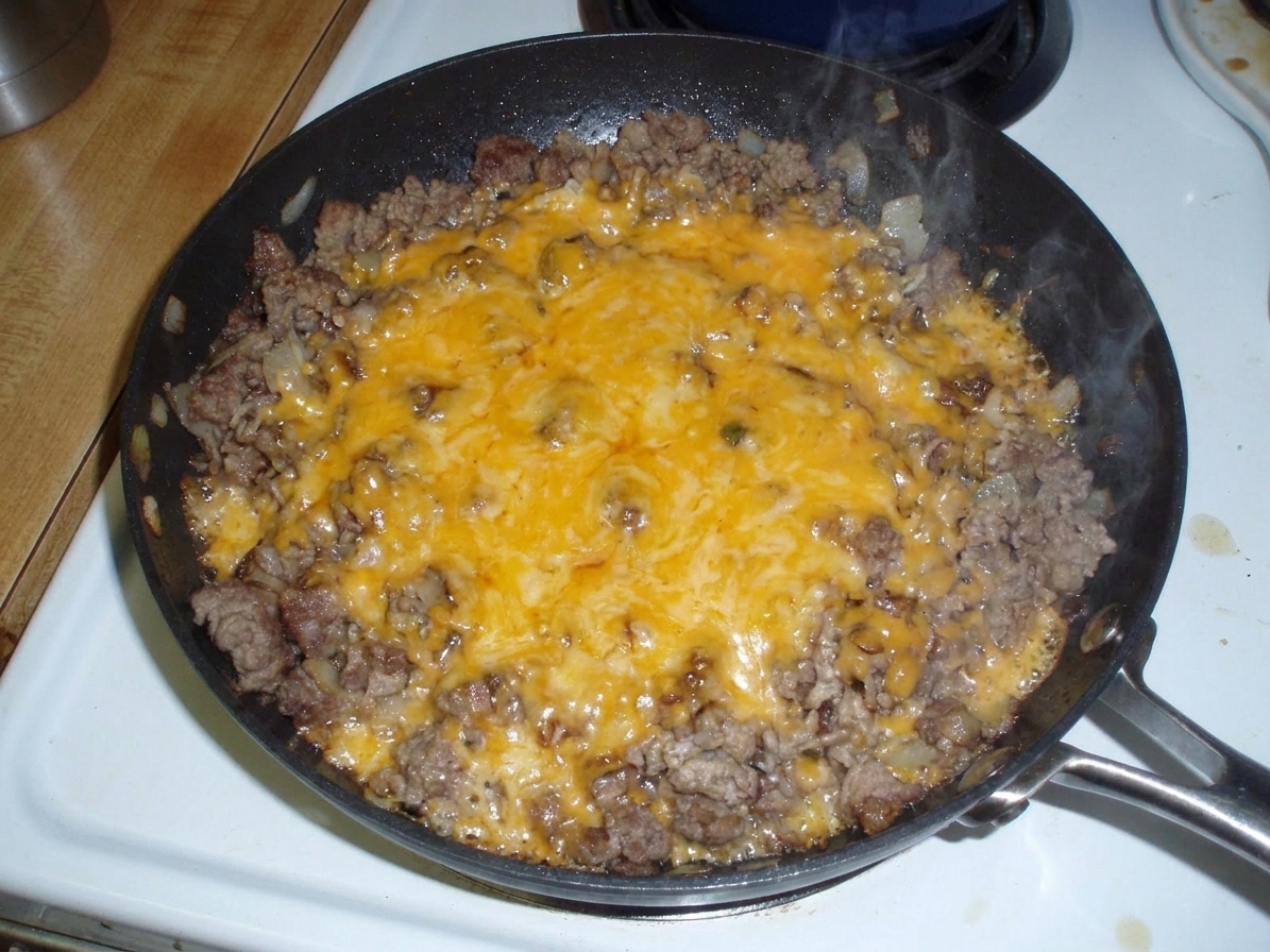 A skillet of taco rice topped with fully melted cheddar cheese, bubbling at the edges on a warm kitchen counter