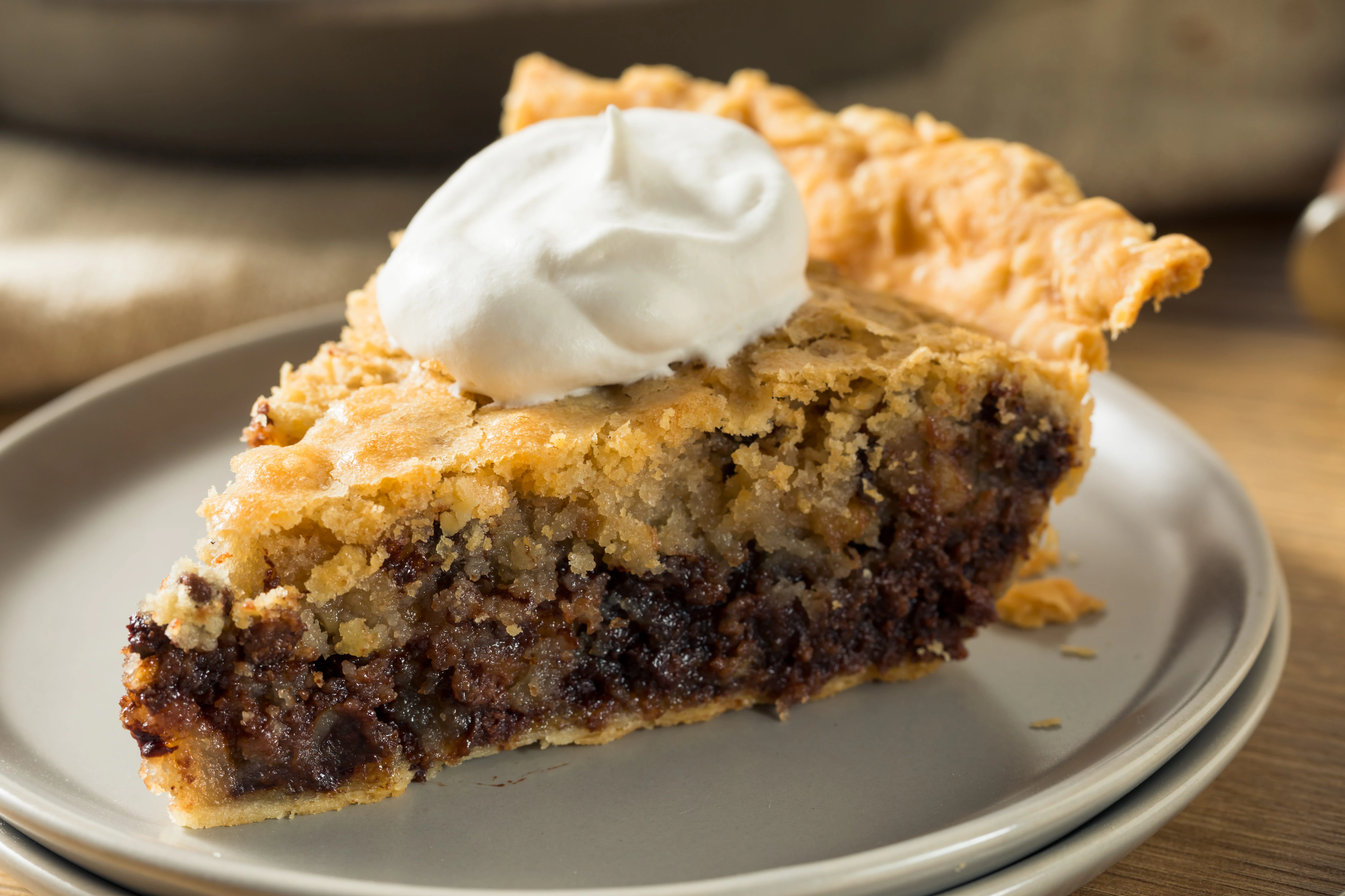 A slice of Kentucky Derby-style pie on a small dessert plate, showing a gooey chocolate chip and walnut filling inside a flaky crust on a warm wood table with soft natural light