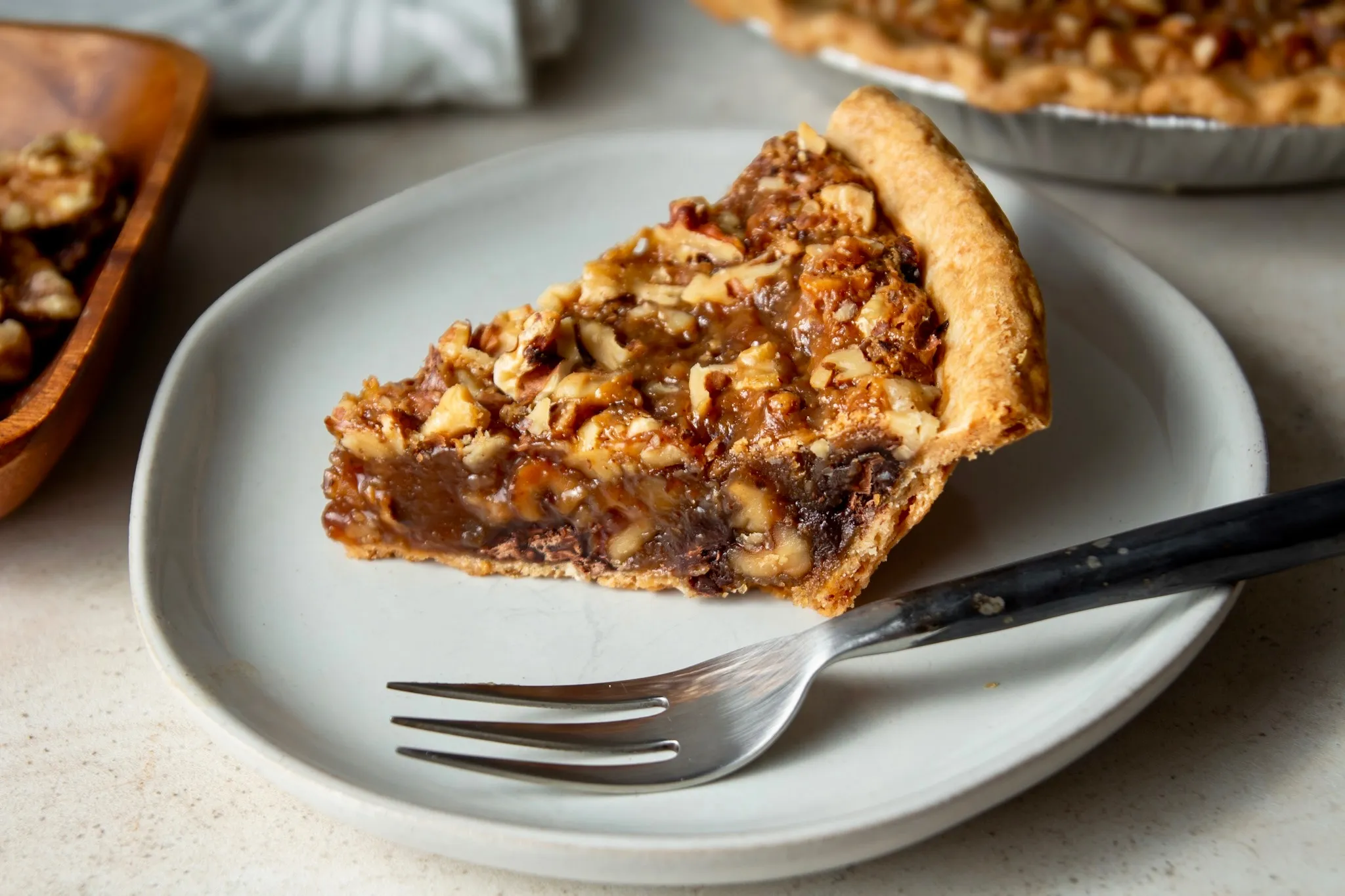 A slice of Kentucky chocolate walnut pie on a dessert plate, showing a fudgy chocolate filling studded with toasted walnuts in a flaky pie crust, warm kitchen lighting