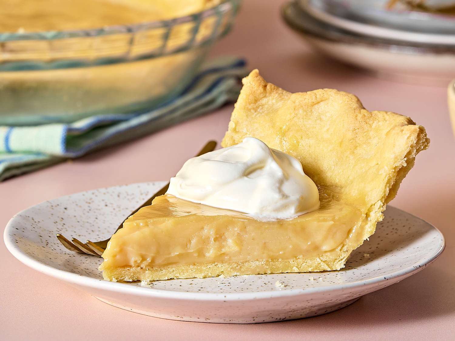 A slice of butterscotch pie with glossy brown sugar custard and a thick layer of whipped cream on top, served on a small dessert plate at a wooden kitchen table with warm natural light
