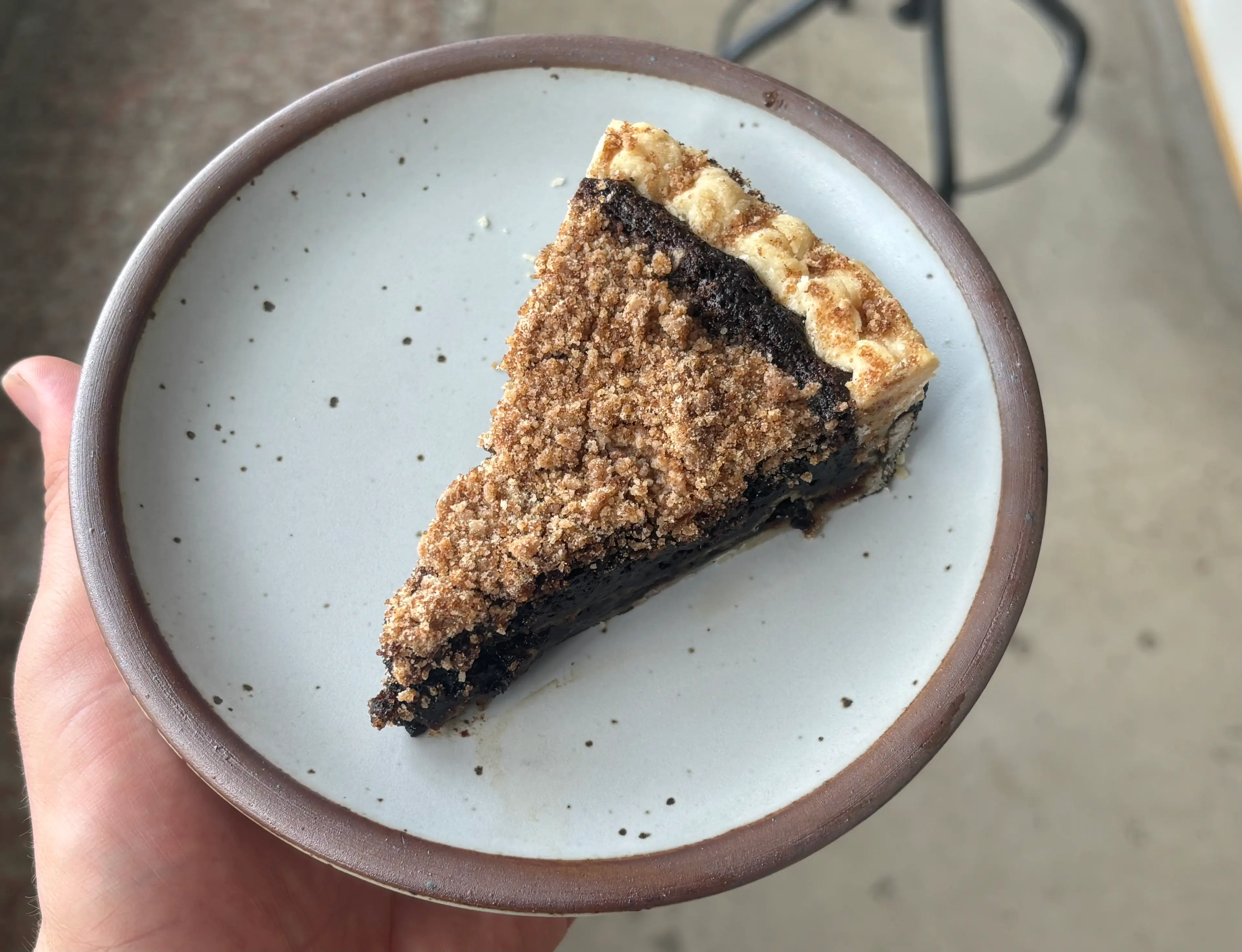 A slice of classic shoofly pie on a small plate, showing a gooey molasses layer under a thick brown sugar crumb topping, with a fork on the side on a warm kitchen table