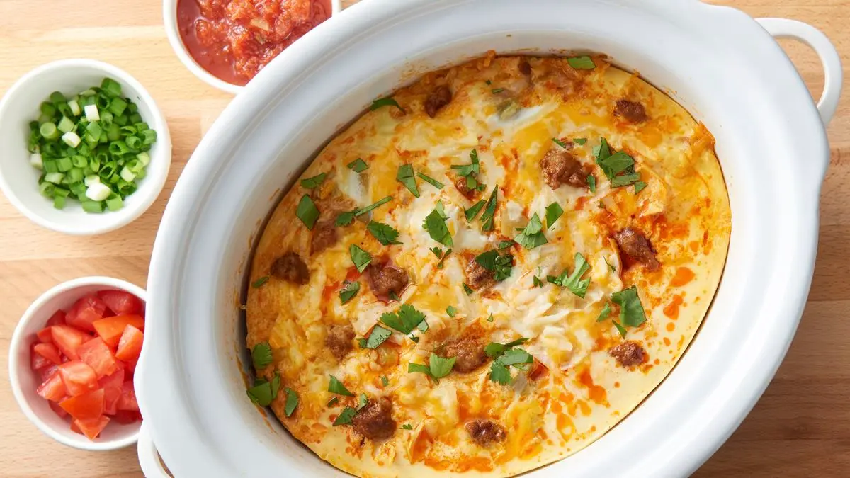 A sliced crockpot breakfast casserole with golden cheese on top, served on a white plate with a fork on a sunlit kitchen table