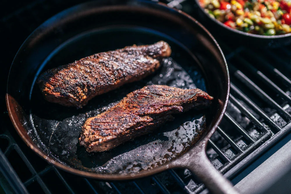 A sliced hanger steak with crisp seared edges on a cutting board, glossy garlic herb butter melting over the slices, with a cast iron skillet nearby on a warm kitchen counter