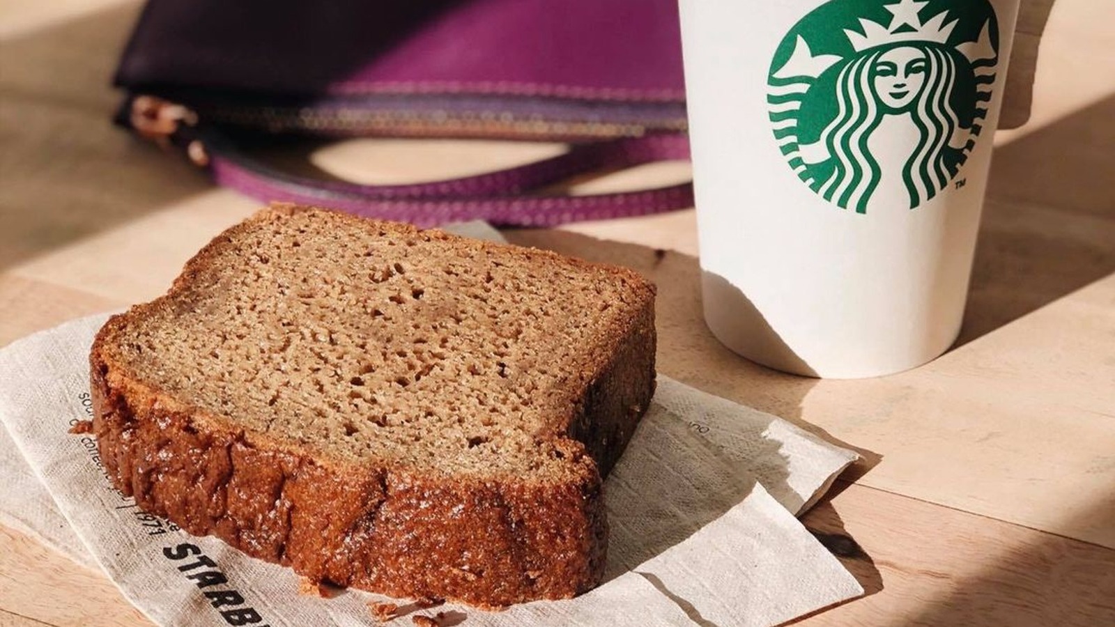 A sliced loaf of Starbucks-style banana bread on a wooden cutting board with a few walnut pieces on top, warm kitchen counter lighting