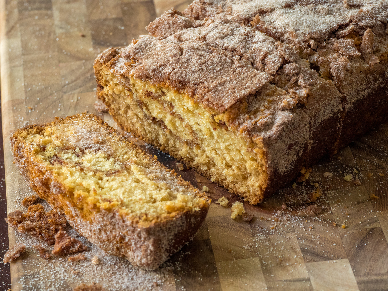 A sliced loaf of cinnamon friendship bread on a wooden cutting board with a crackly cinnamon-sugar top, warm kitchen counter light