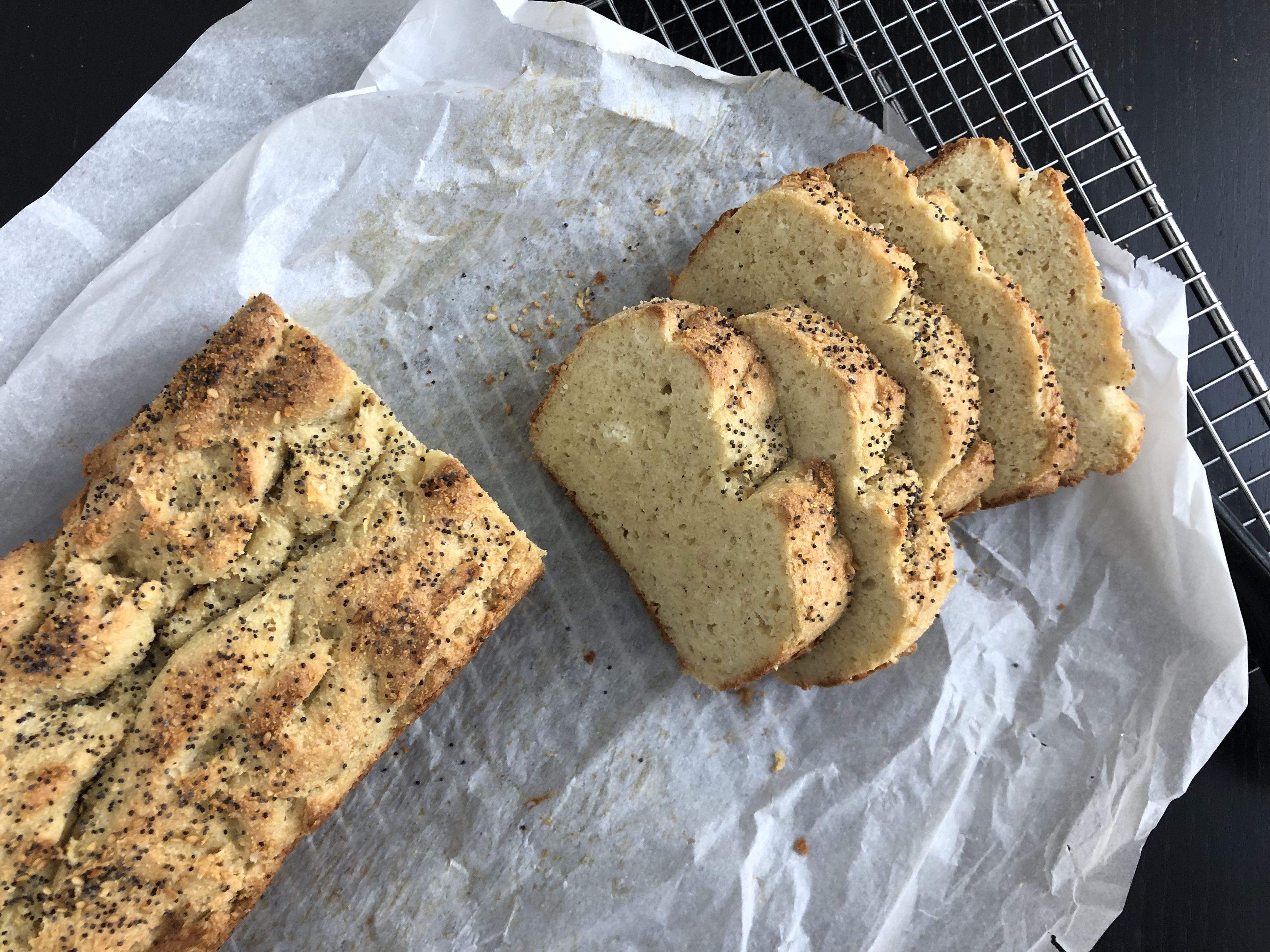 A sliced loaf of low carb almond flour bread on a wooden cutting board with a few slices fanned out in warm kitchen lighting