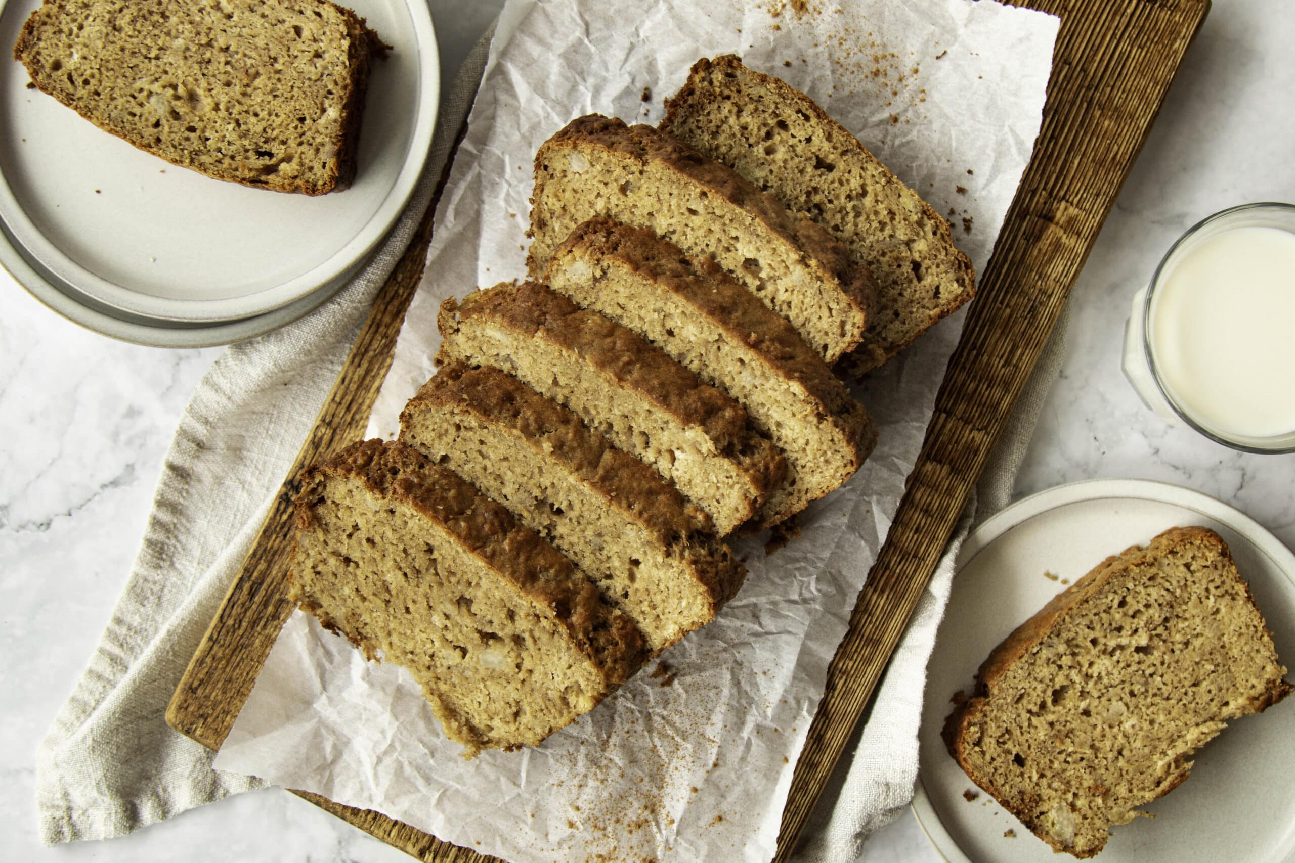 A sliced loaf of protein banana bread on a wooden cutting board with banana slices nearby in a bright home kitchen