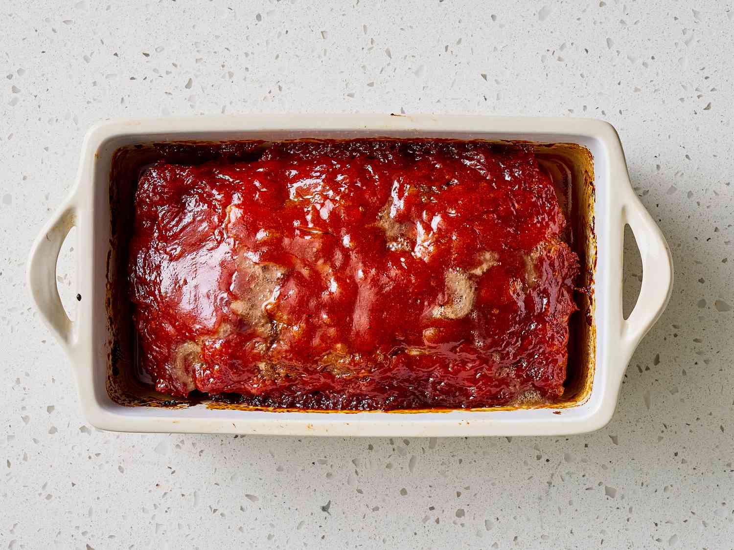 A sliced old fashioned meatloaf with a glossy ketchup glaze on top, arranged on a serving platter on a warm kitchen table