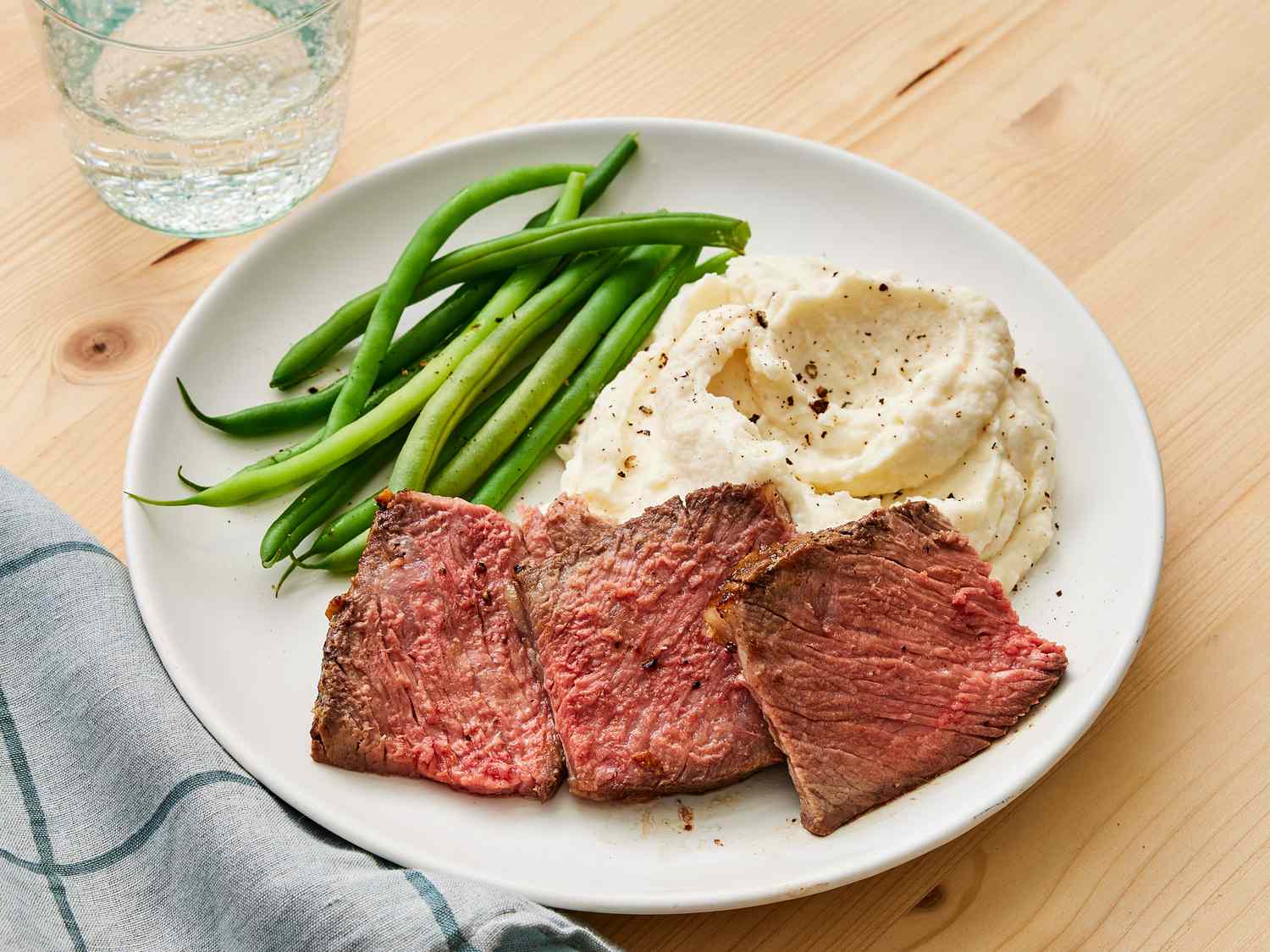 A sliced ribeye roast fanned on a warm platter with a browned crust, rosy medium-rare center, and a small bowl of pan sauce on a cozy dinner table