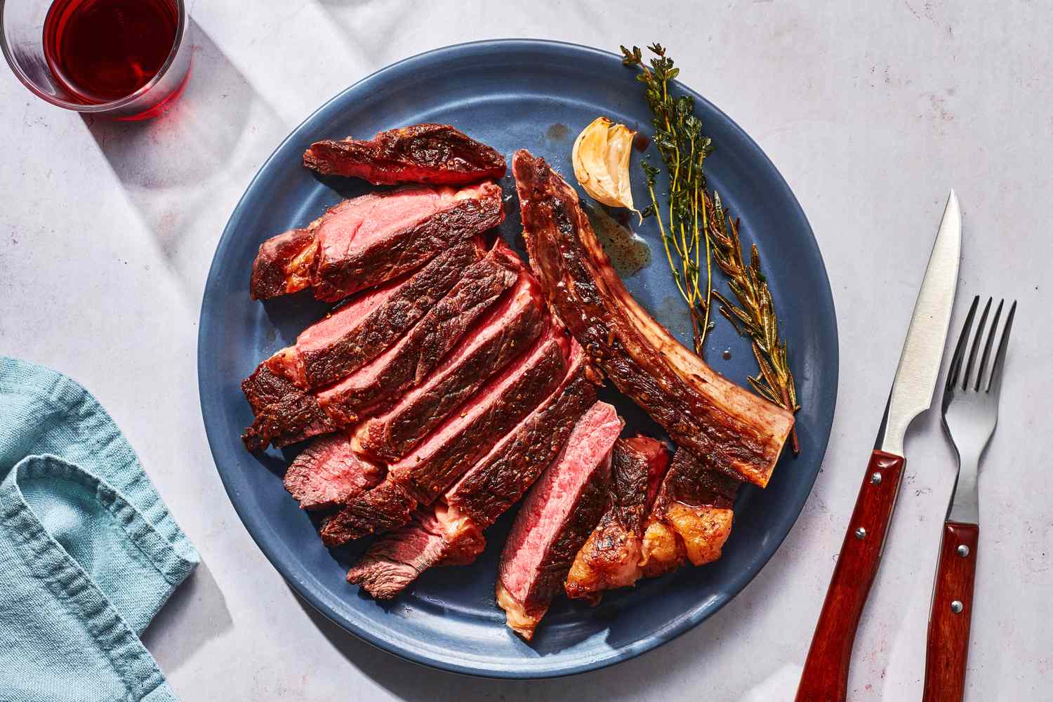 A sliced ribeye roast fanned on a white platter with browned crust, juicy pink center, and rosemary sprigs on a warm kitchen table
