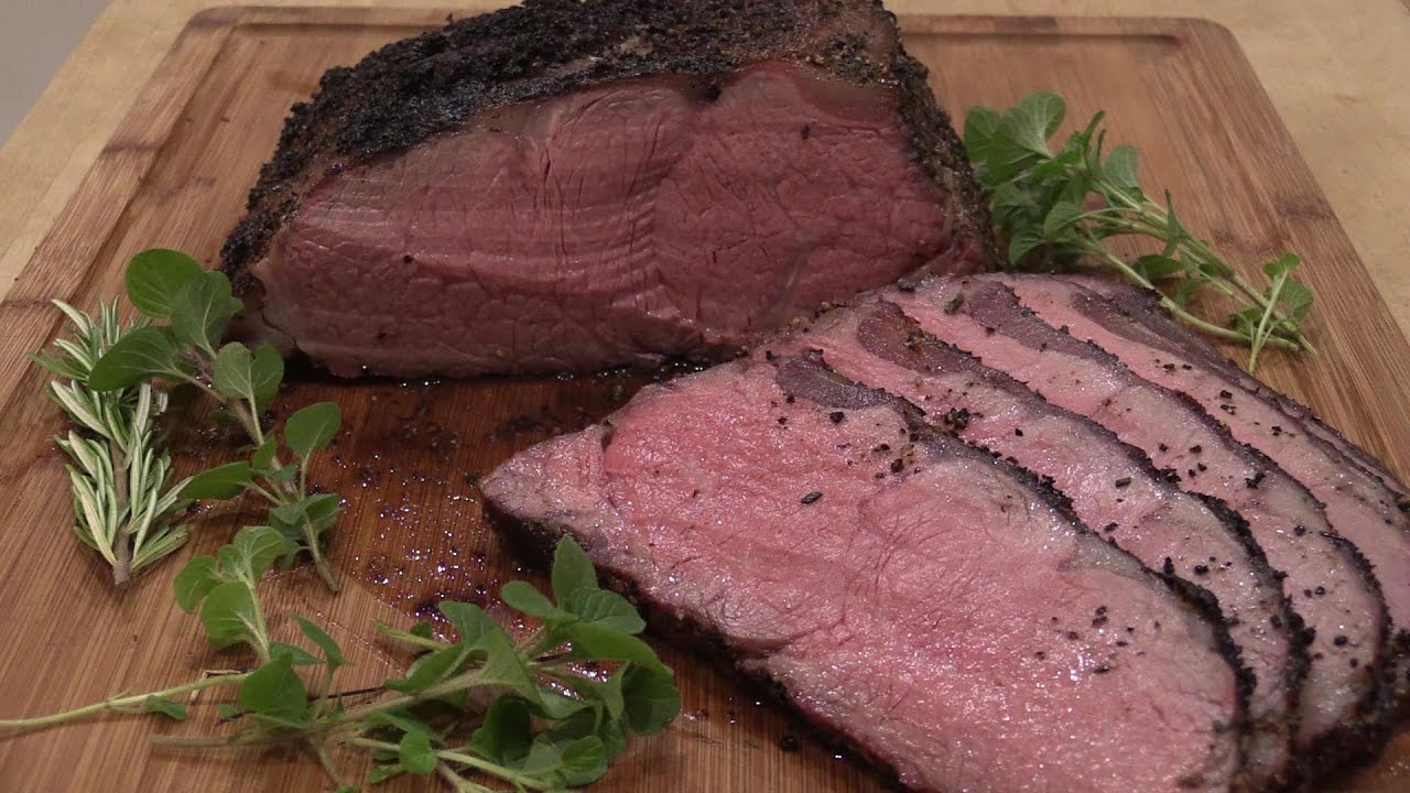 A sliced shell steak roast on a cutting board with a browned crust, rosy medium-rare center, and a small bowl of pan sauce nearby on a warm kitchen counter