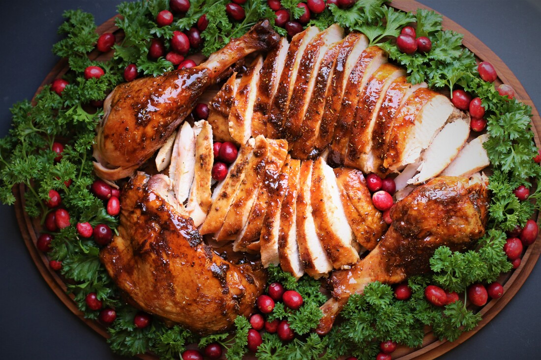 A sliced smoked turkey breast fanned out on a platter with herbs and lemon on a rustic wooden table in warm natural kitchen lighting