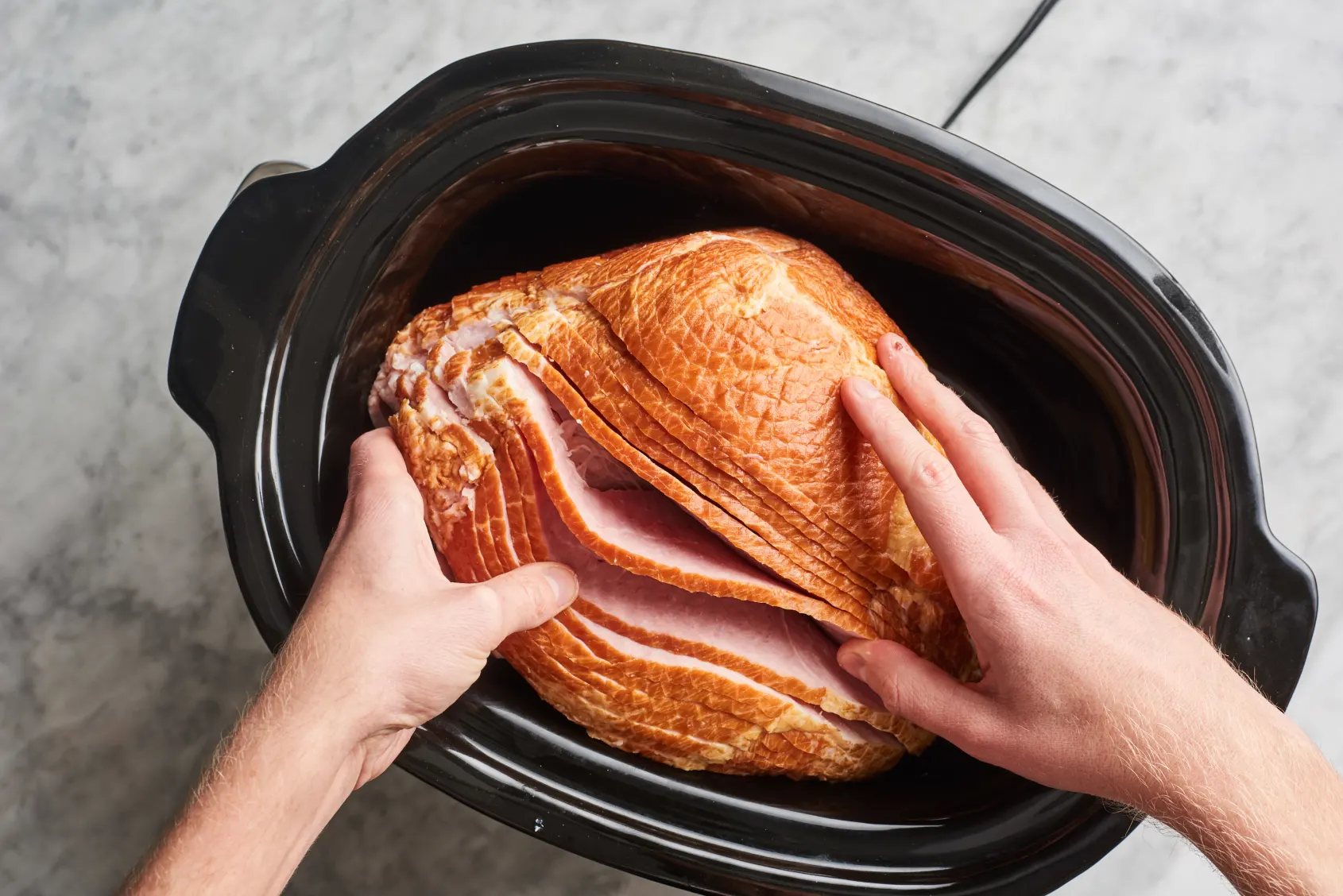 A sliced spiral ham sitting in a slow cooker with a glossy brown sugar glaze pooling at the bottom on a bright kitchen counter