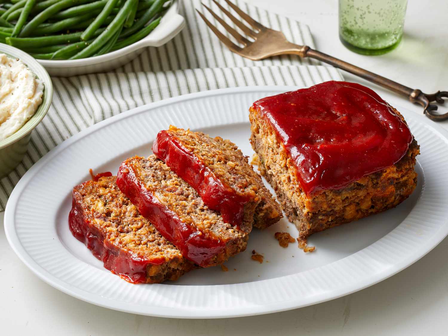 A sliced stove top stuffing meatloaf on a cutting board with a glossy ketchup-brown sugar glaze on a cozy kitchen counter