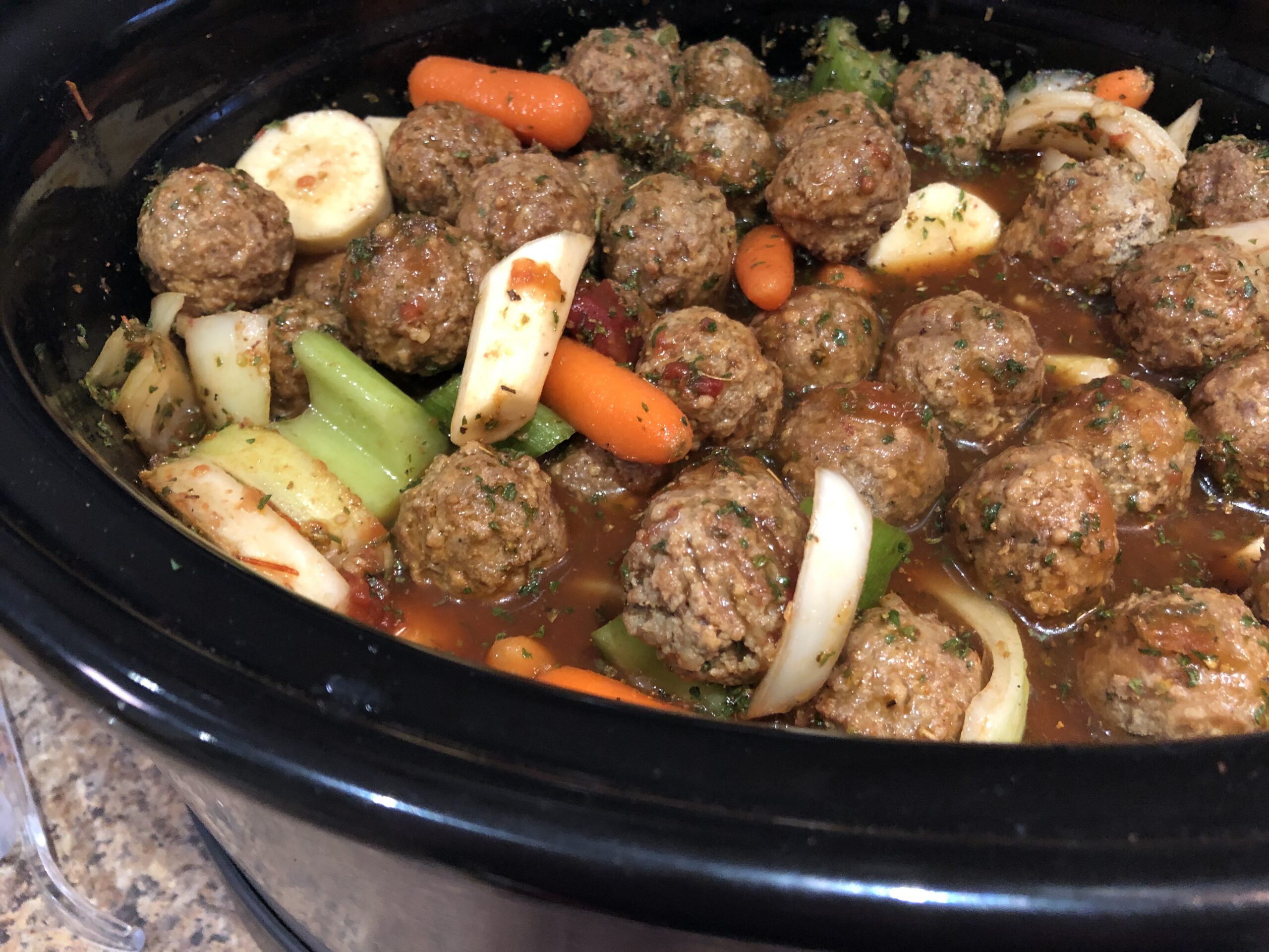A slow cooker filled with saucy cocktail meatballs, a small ladle resting inside, on a clean kitchen counter