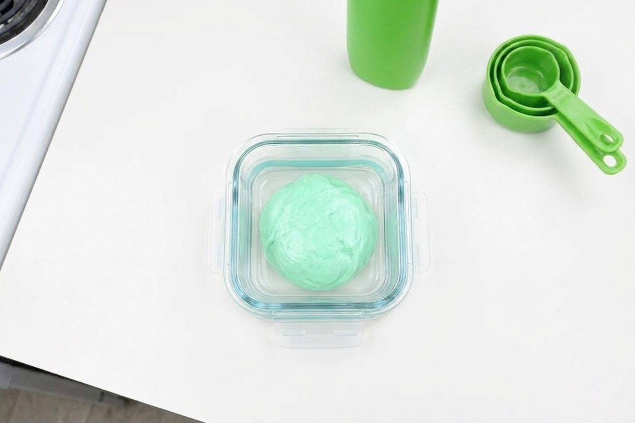 A small airtight container holding a ball of homemade slime on a kitchen counter
