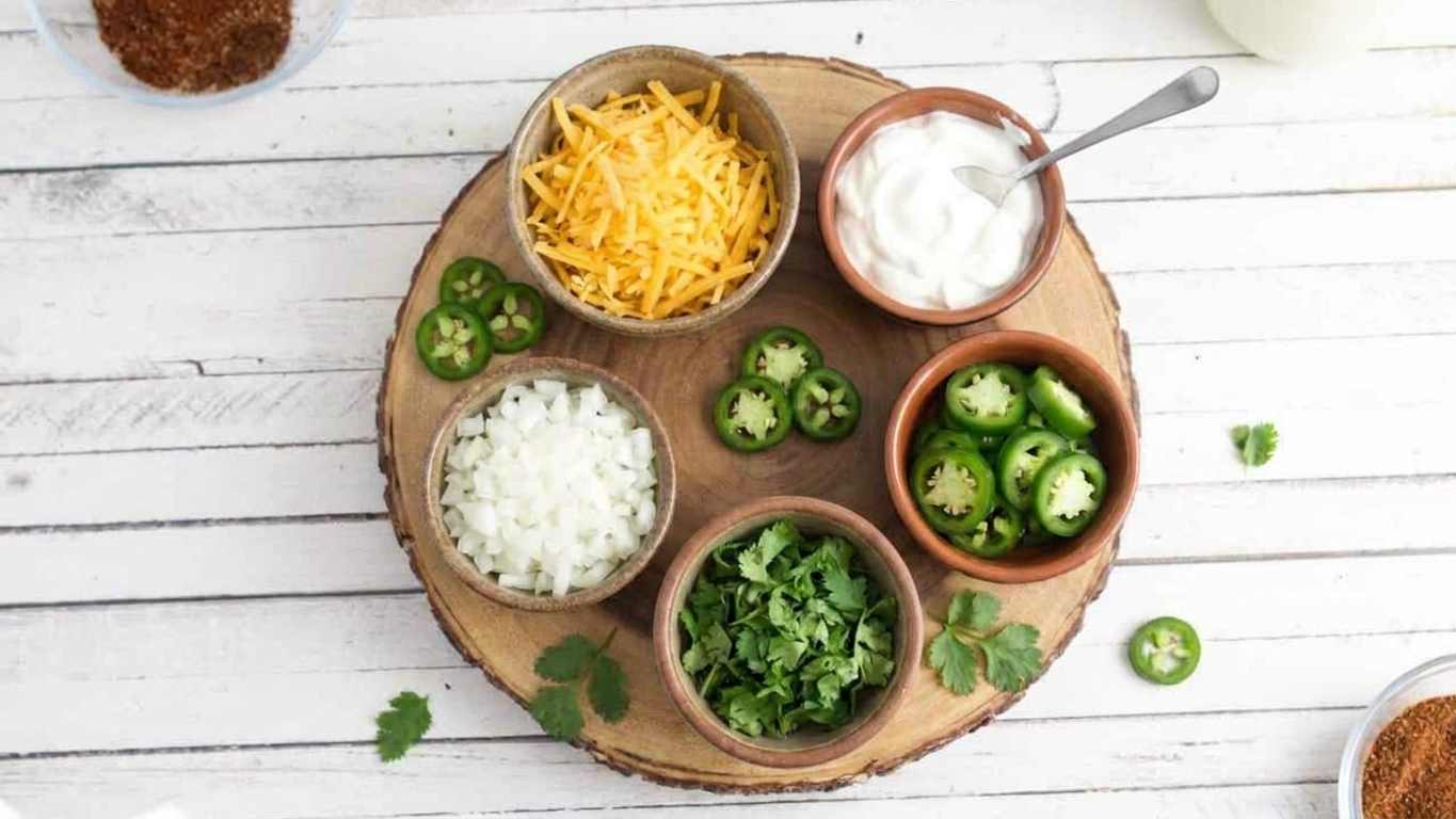 A small board with bowls of chili toppings including shredded cheese, sour cream, diced onions, jalapeños, and cilantro on a kitchen counter