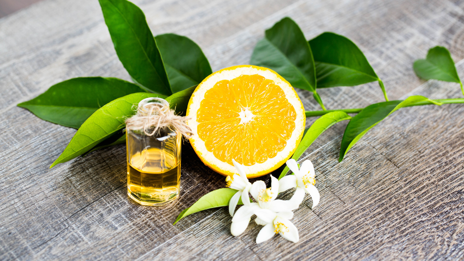 A small bottle of orange blossom water beside an orange, a lemon, and a microplane on a bright kitchen counter