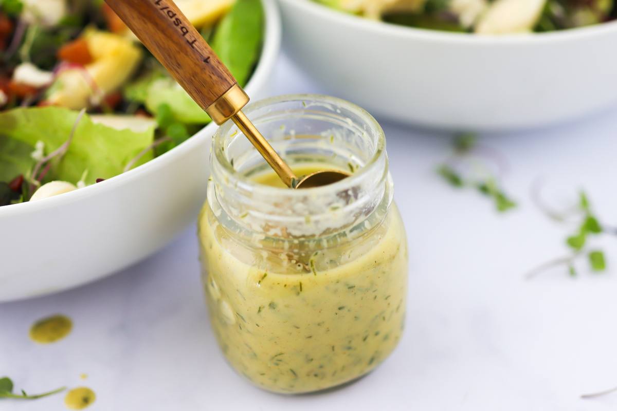 A small bowl of Dijon mustard herb sauce with chopped parsley and a whisk on a light kitchen counter