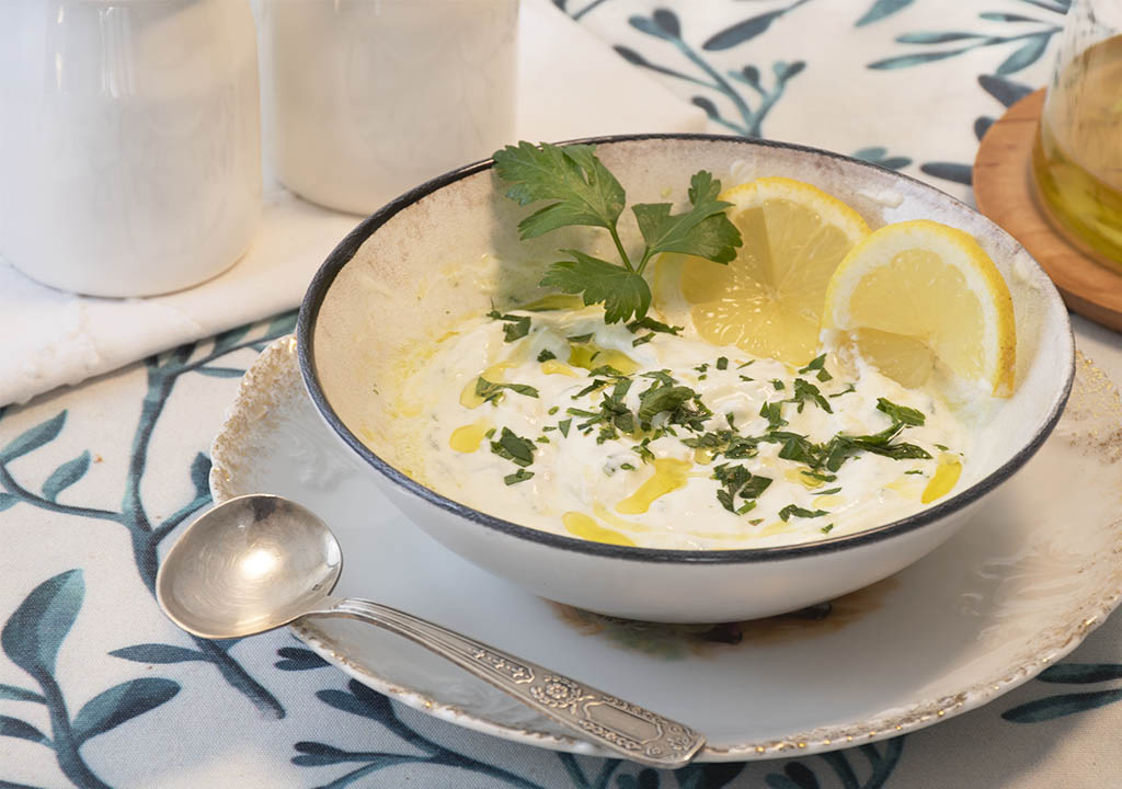 A small bowl of Greek yogurt being stirred with lemon juice and grated garlic on a kitchen counter