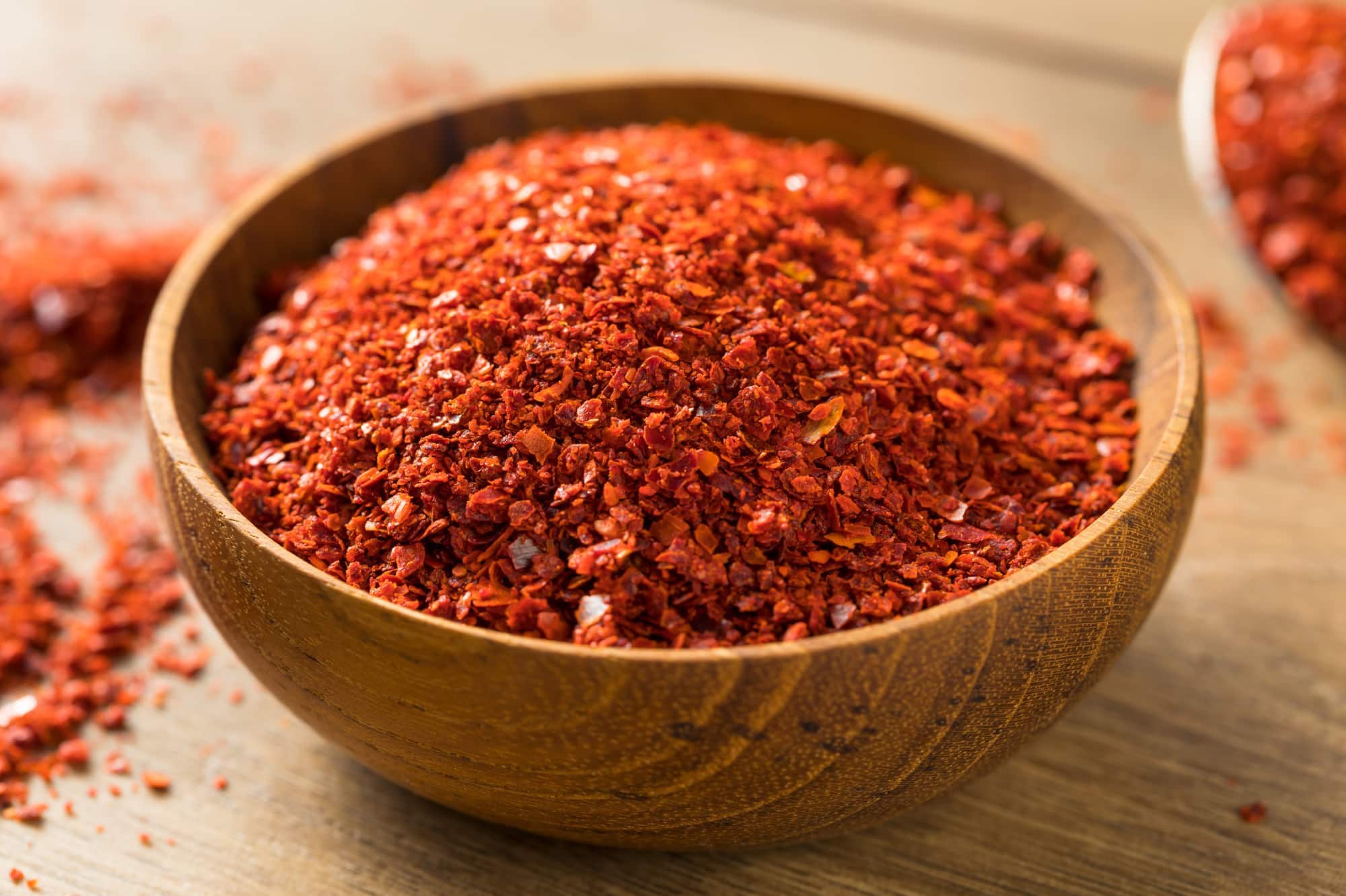 A small bowl of Korean gochugaru red pepper flakes next to garlic, sesame oil, and rice vinegar on a tidy kitchen counter