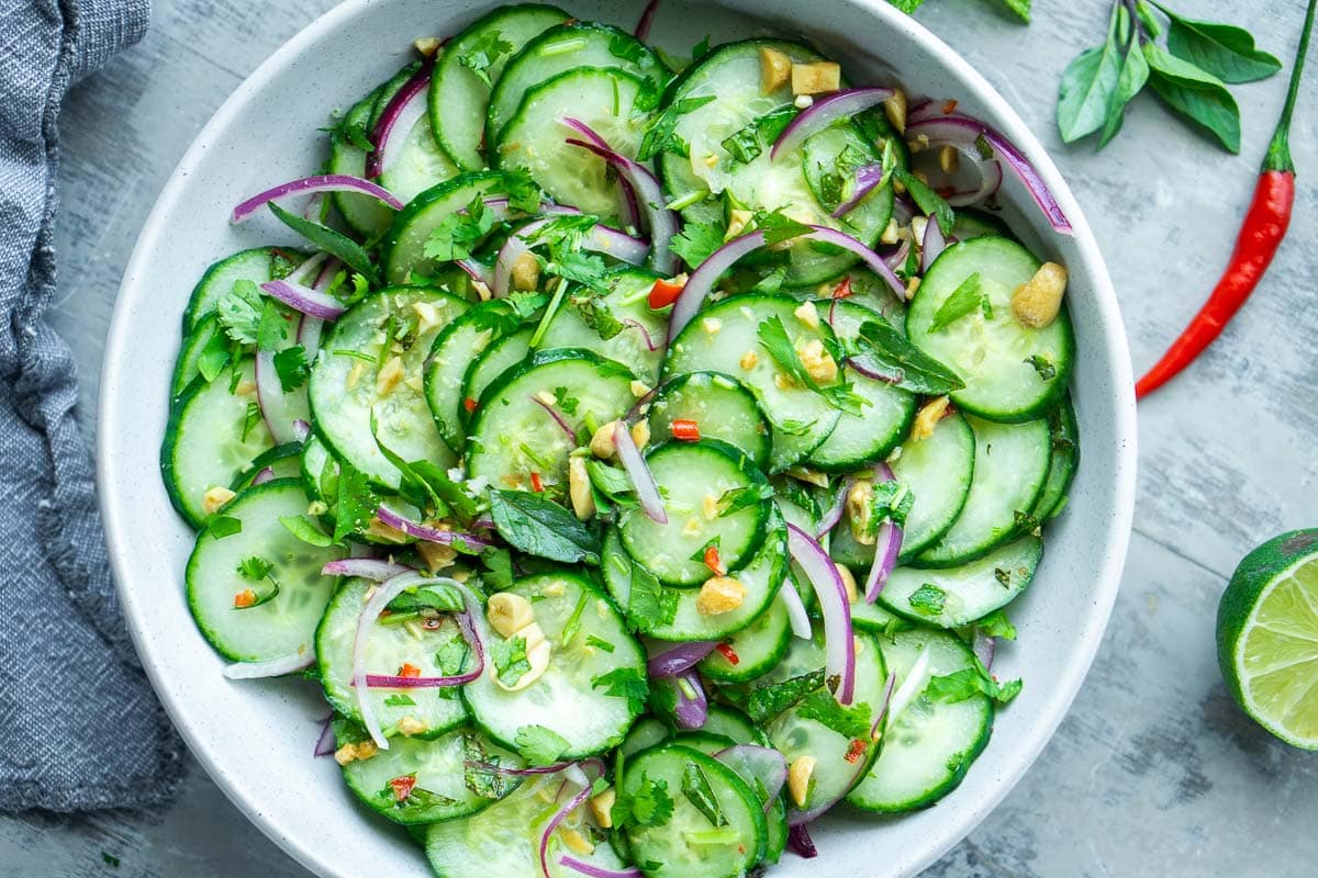 A small bowl of Thai-style cucumber salad with thinly sliced cucumbers, red onion, and cilantro in a light dressing, photorealistic food photography