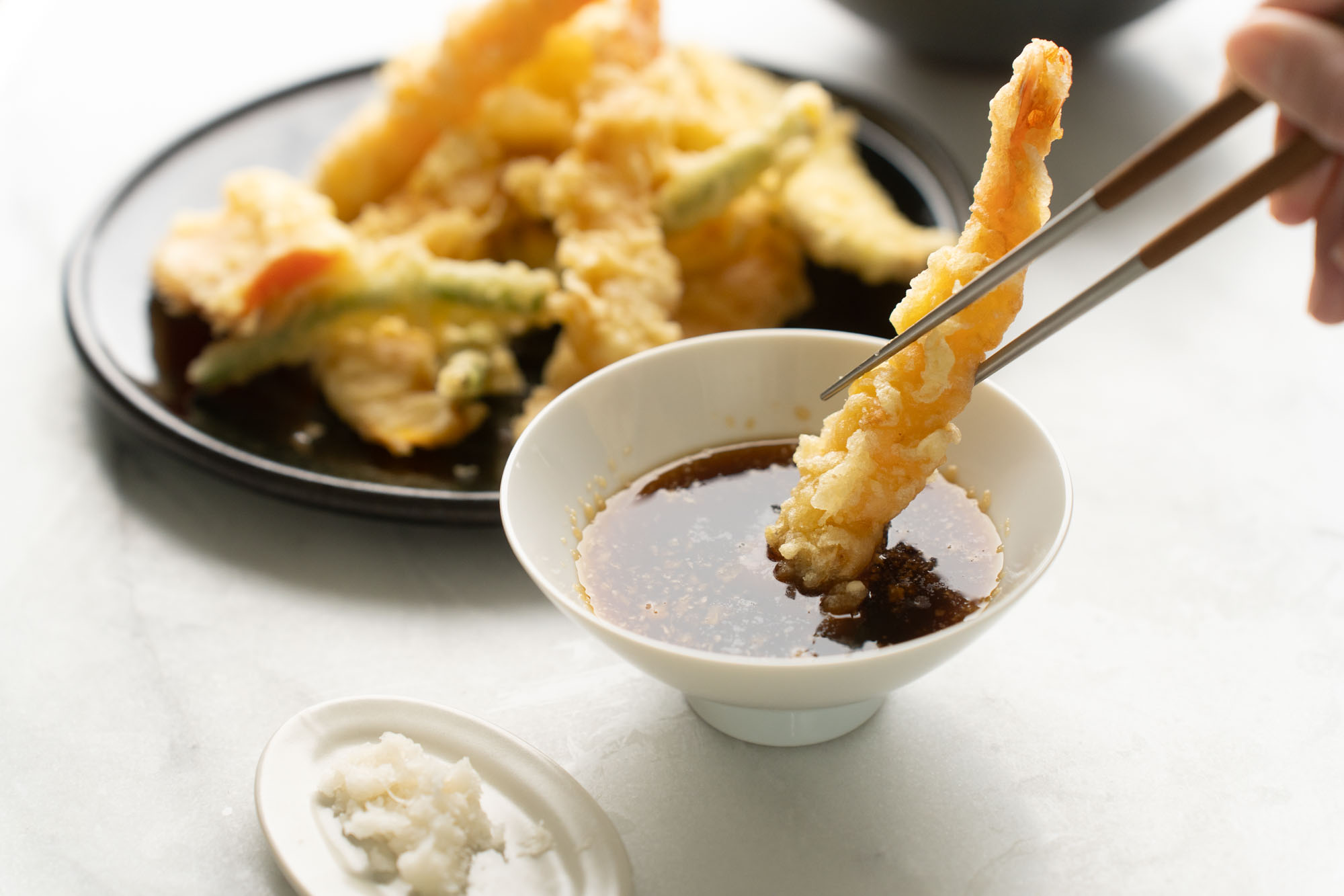 A small bowl of amber tempura dipping sauce topped with grated daikon and sliced green onion on a kitchen counter
