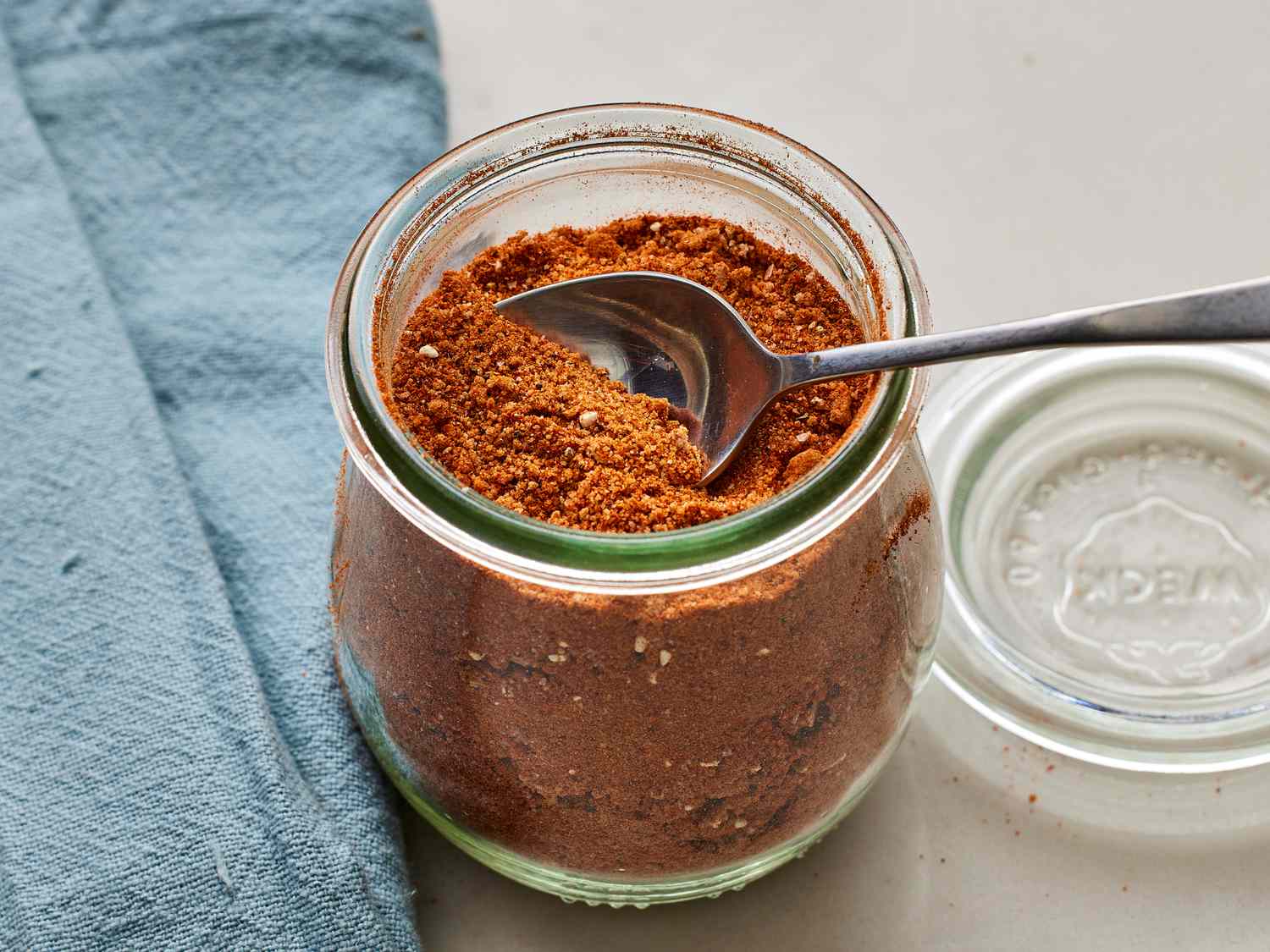 A small bowl of brown sugar and spice rub with smoked paprika and garlic powder on a kitchen counter next to measuring spoons