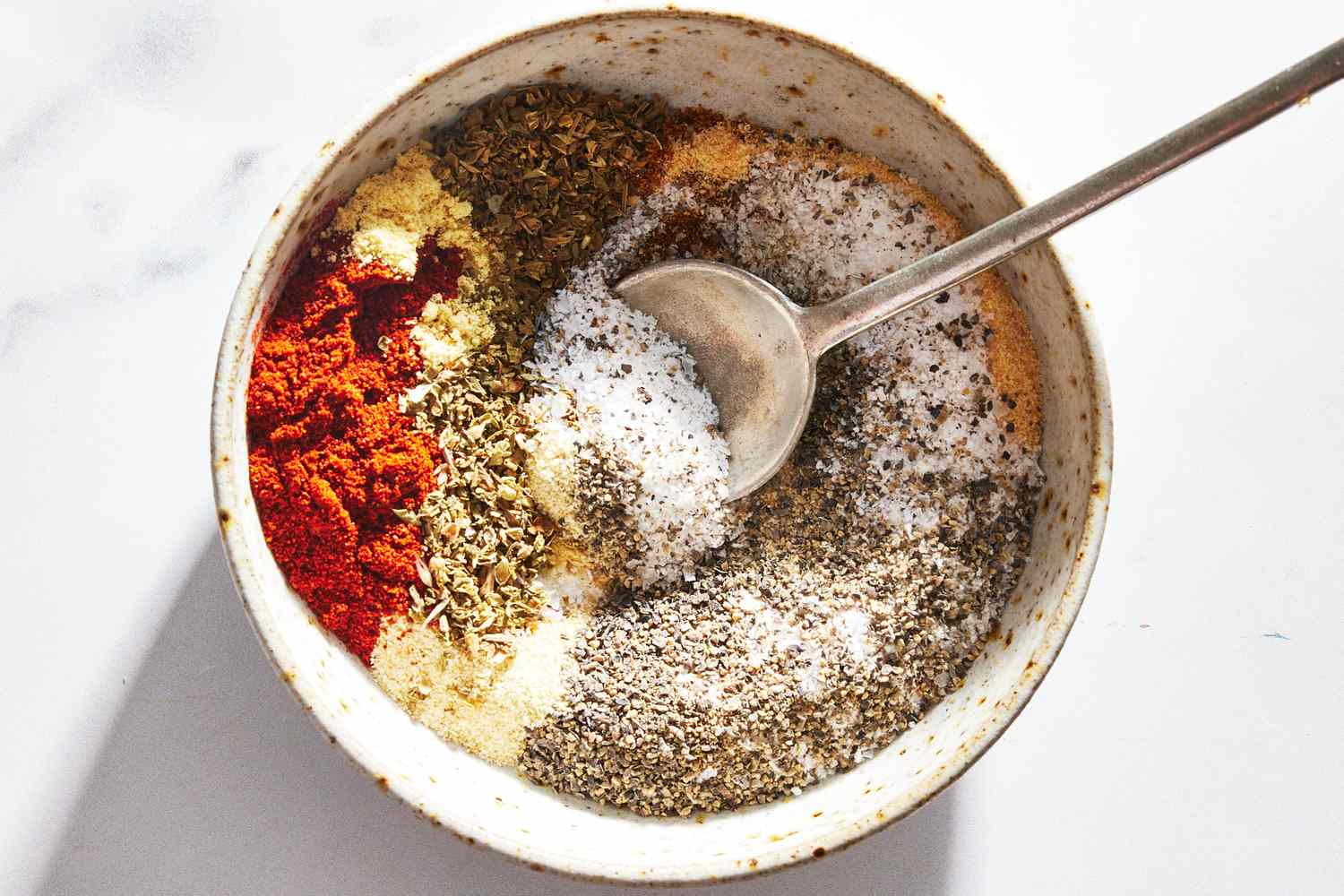 A small bowl of chicken spice rub with smoked paprika, garlic powder, and black pepper on a kitchen counter next to measuring spoons