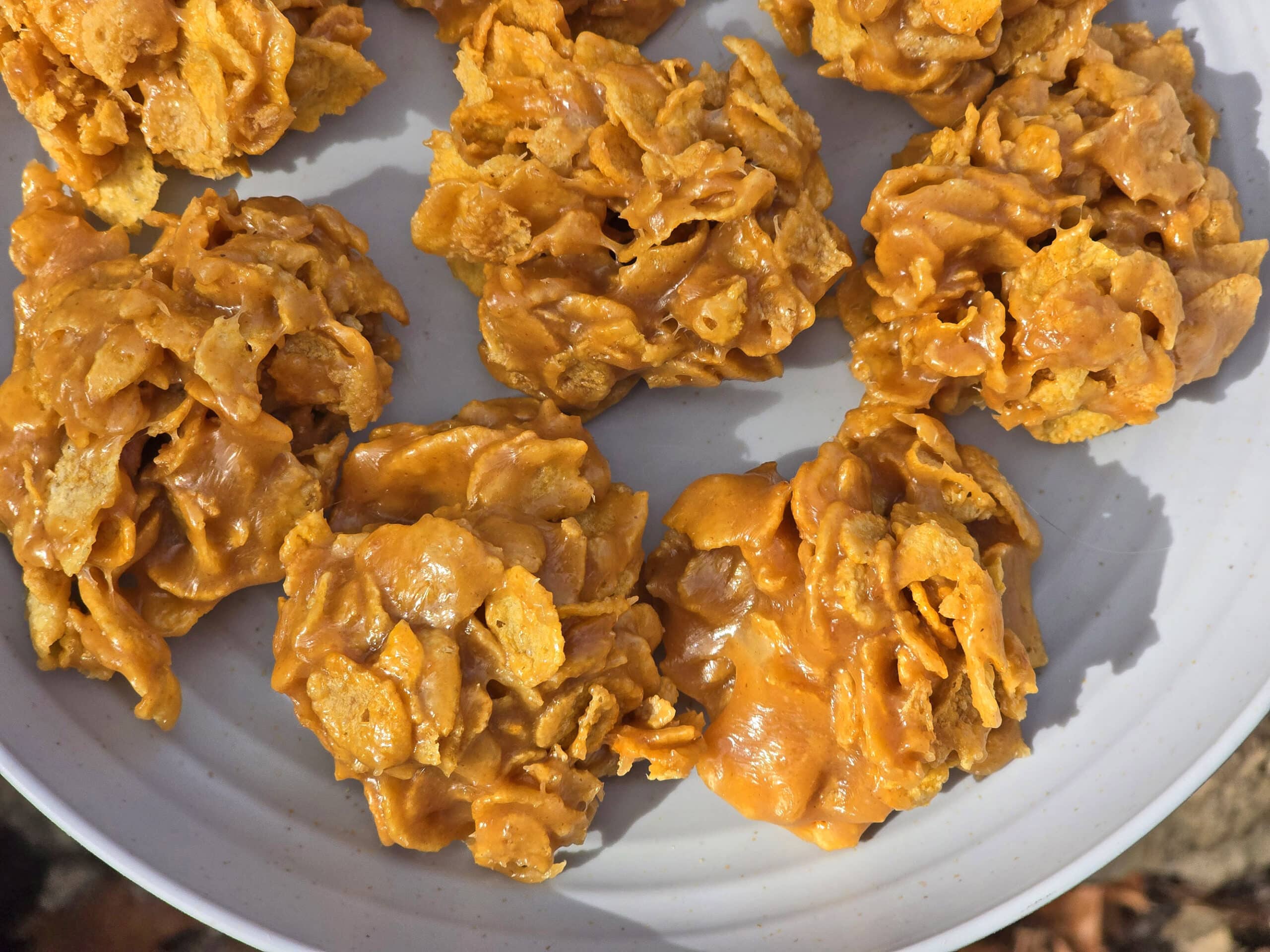 A small bowl of crushed cornflakes being mixed with melted butter, sugar, and cinnamon on a kitchen counter