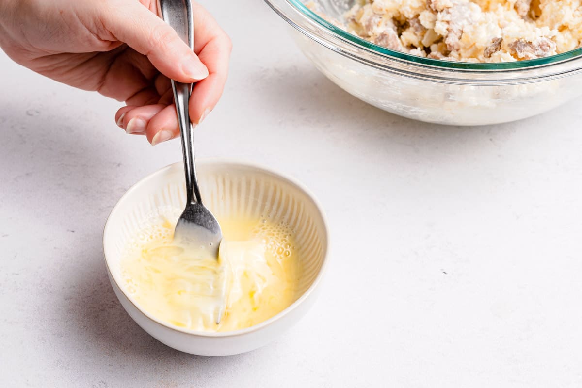 A small bowl of egg wash being whisked with a fork on a kitchen counter