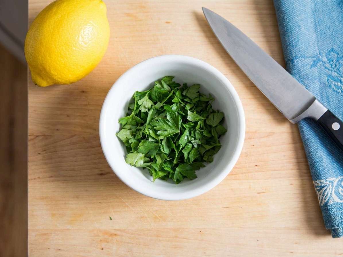 A small bowl of freshly chopped flat-leaf parsley on a kitchen counter next to a lemon and a knife