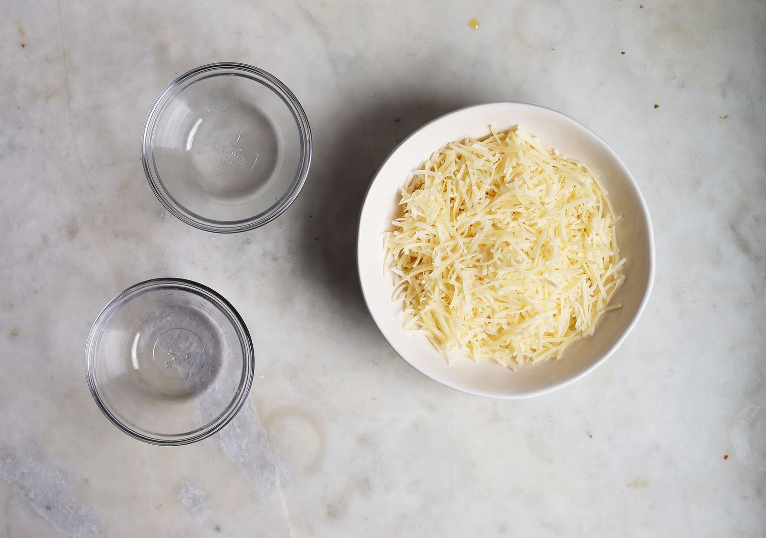 A small bowl of freshly grated Parmesan cheese on a wooden cutting board beside a microplane grater