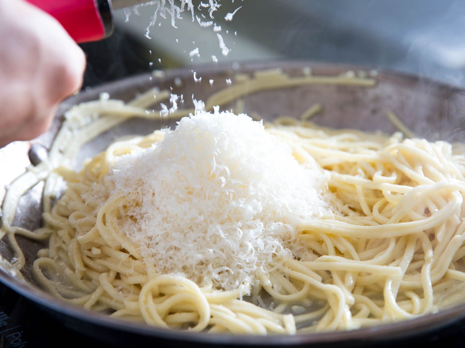 A small bowl of freshly grated Parmesan cheese on a kitchen counter next to a microplane grater