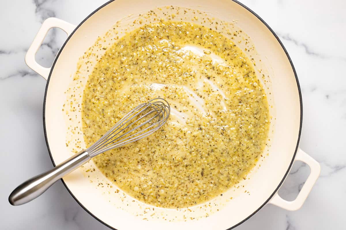 A small bowl of freshly grated Parmesan, minced garlic, and butter next to a skillet on a stovetop, ready to cook