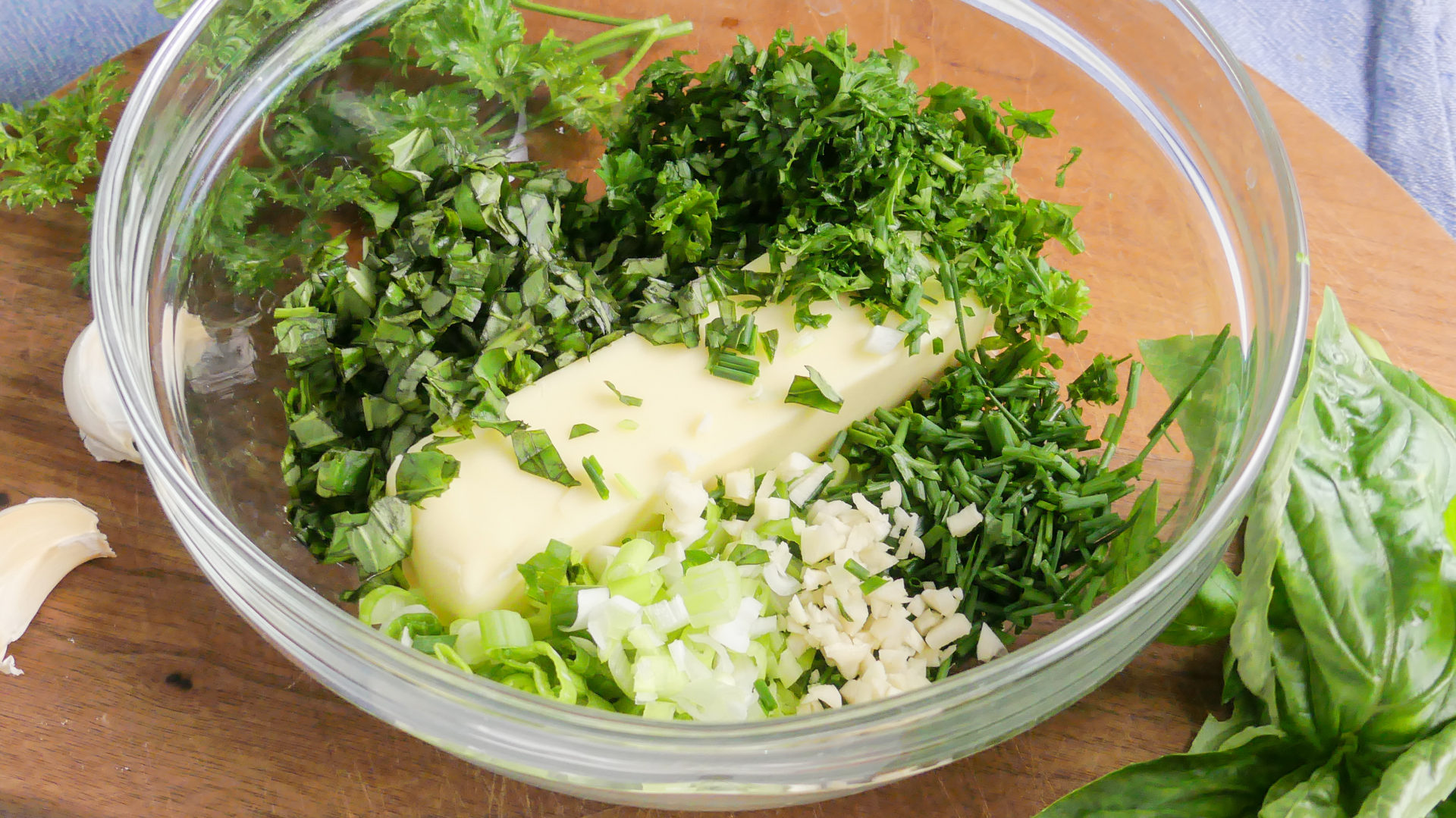 A small bowl of garlic butter mixed with parsley on a kitchen counter with a spoon resting inside