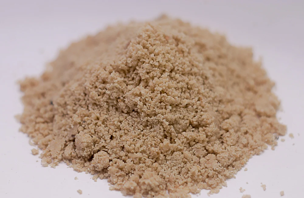 A small bowl of ground egusi powder on a kitchen counter with a spoon beside it, ready to be mixed into a paste