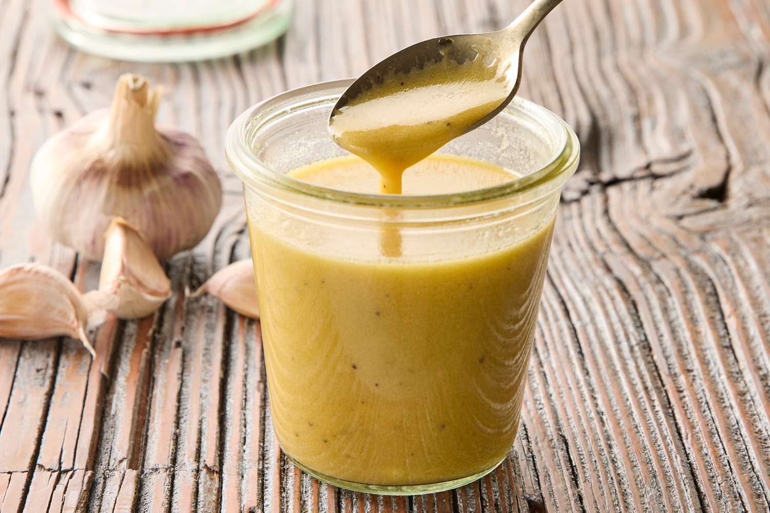 A small bowl of honey Dijon garlic sauce being whisked with a fork on a kitchen counter