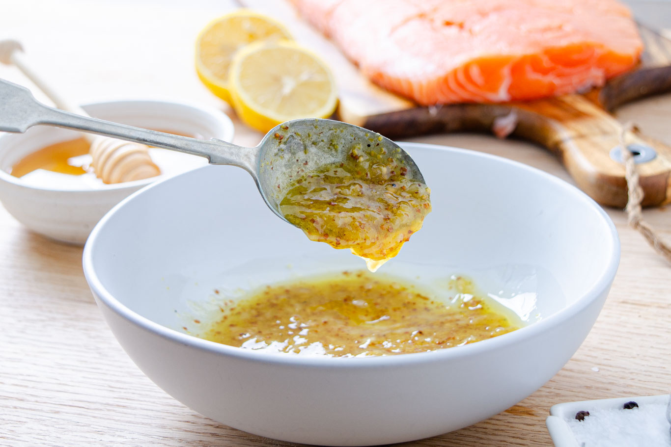 A small bowl of honey mustard glaze being whisked with Dijon, honey, garlic, and lemon juice on a light-colored kitchen counter