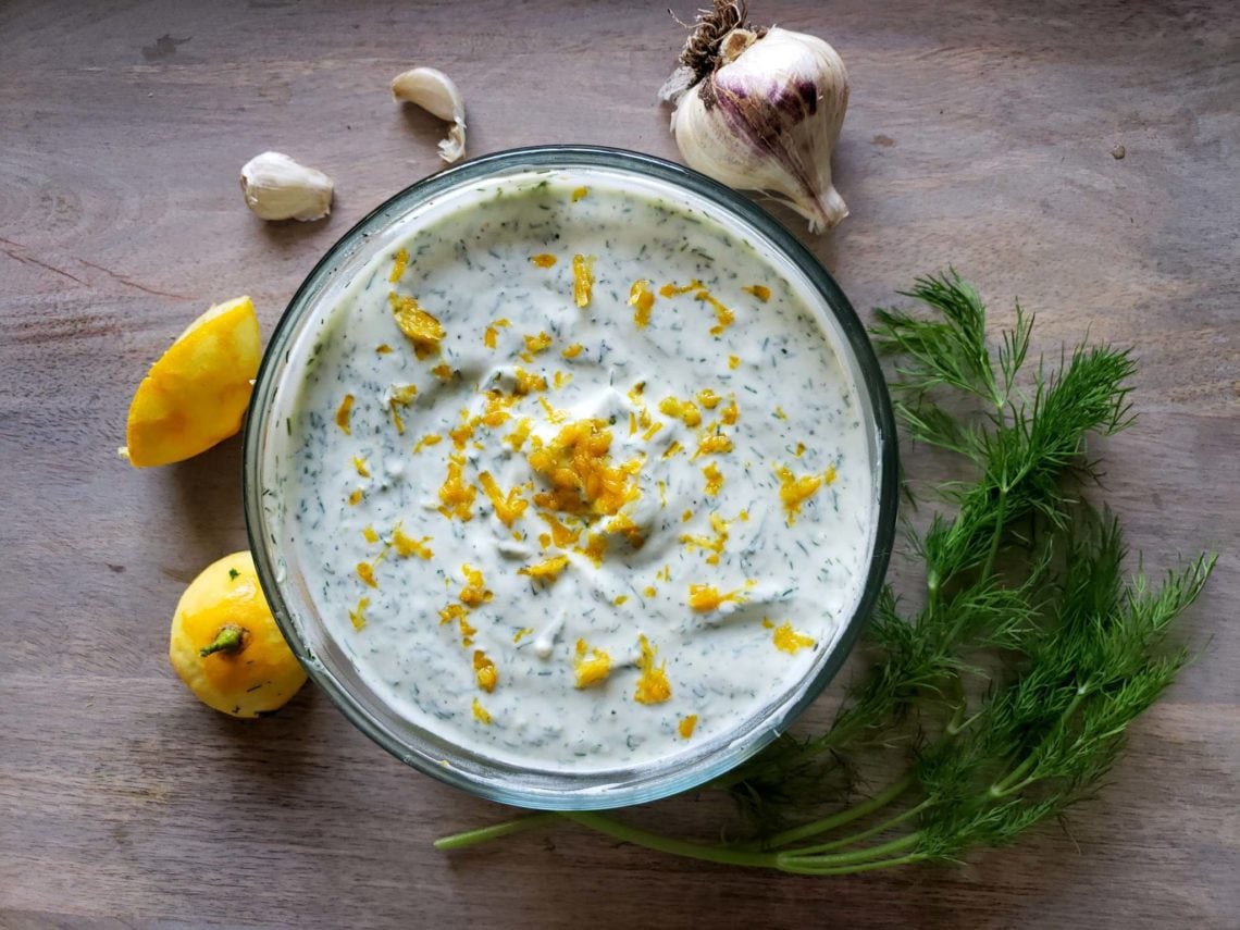 A small bowl of lemon-dill yogurt sauce being stirred with a spoon on a kitchen counter
