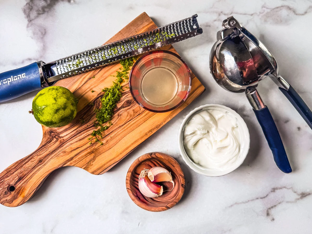 A small bowl of lime crema being whisked on a kitchen counter with a lime and microplane nearby
