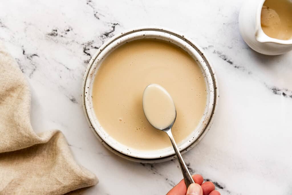 A small bowl of melted butter and maple syrup being whisked with brown sugar and spices on a kitchen counter